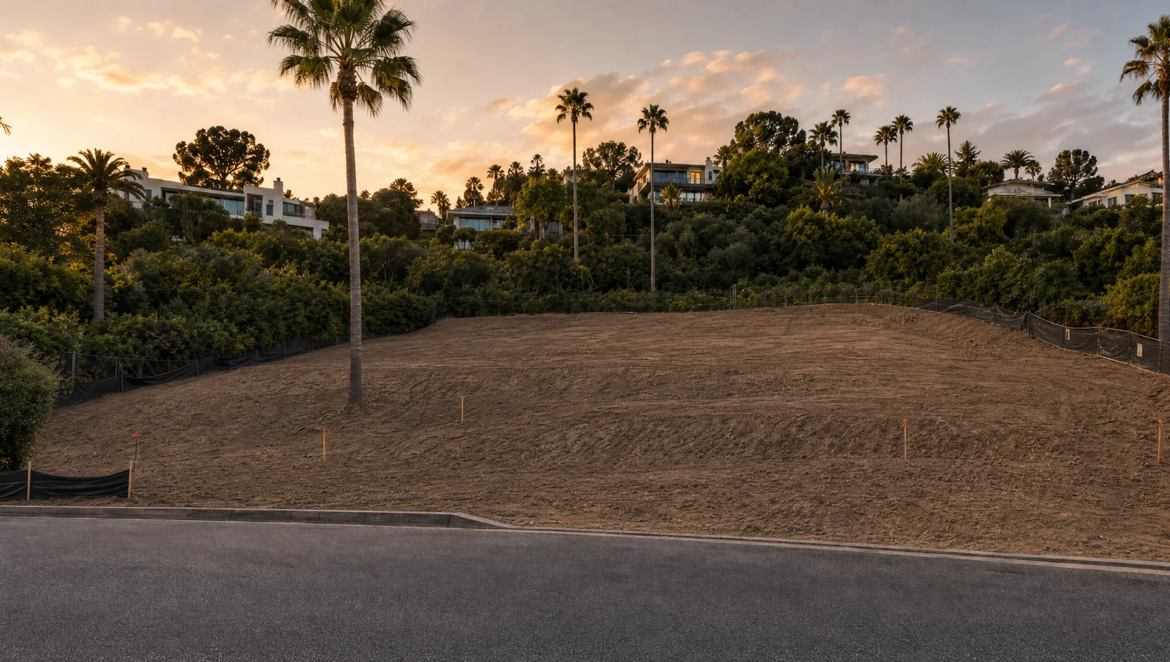 Empty graded hillside lot at golden hour with survey stakes
