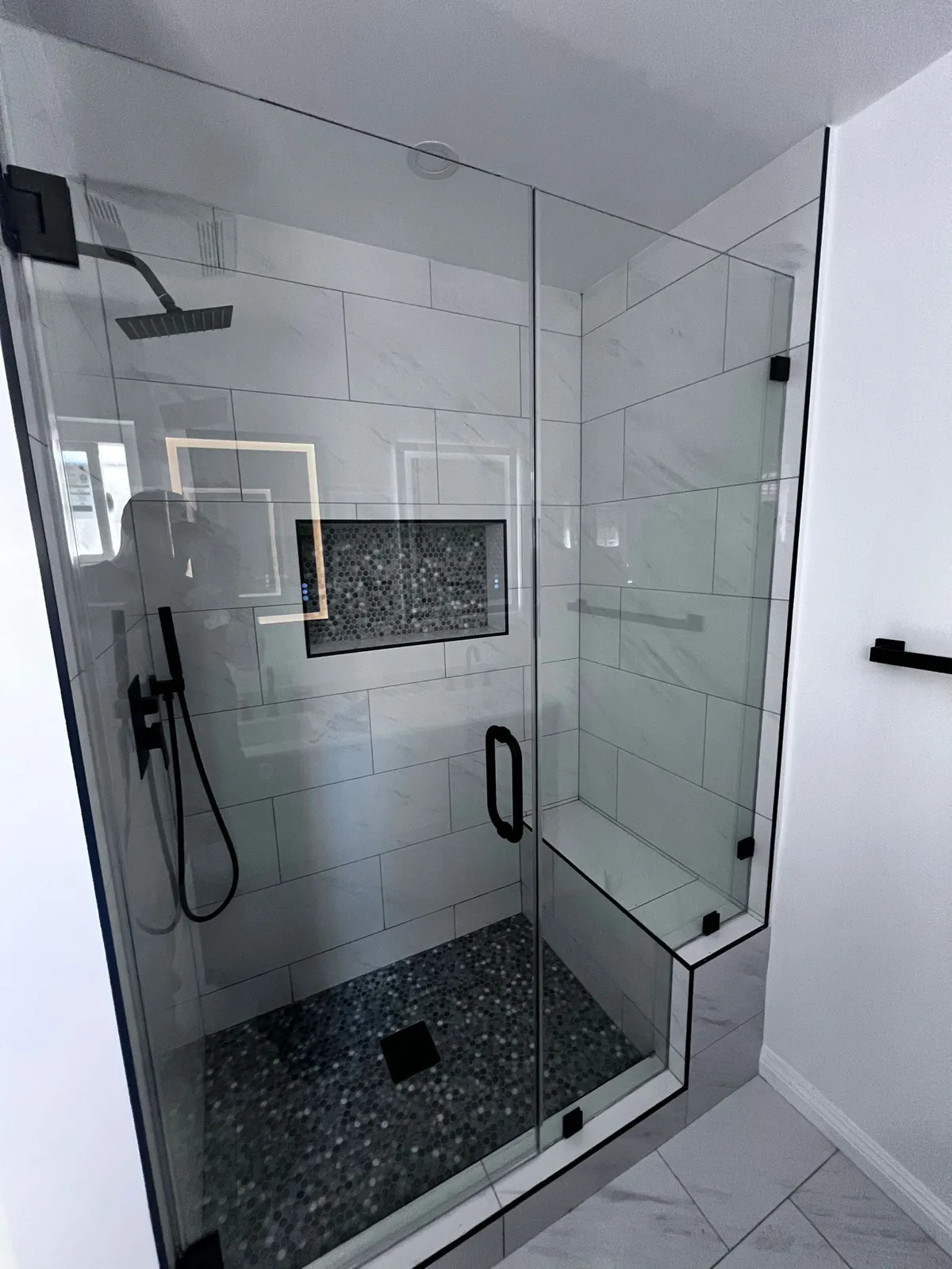 Glass walk-in shower with bench, mosaic niche and pebble floor